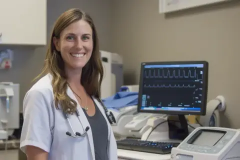 Uśmiechnięta lekarka przy monitorze EKG. Czy nerwica serca wyjdzie na EKG? Zależy od objawów.