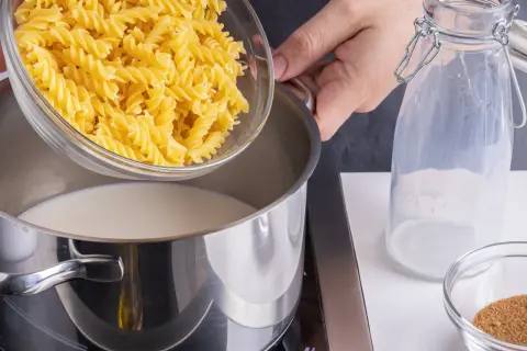 Eine Hand schüttet Spiralnudeln in einen Topf mit Milch. Zutaten für milch nudeln.
