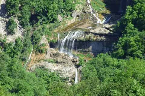 La cascade de la Charabotte dévale une falaise rocheuse, entourée d'une végétation luxuriante. L'eau forme de multiples bras sur les rochers.