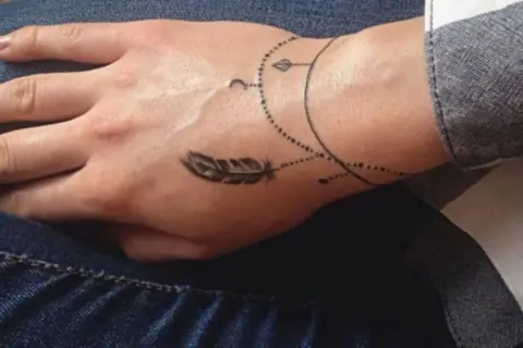 Delikatny, malutki tatuaż na nadgarstku w kształcie piórka i księżyca, ozdobiony kropkami i liniami.