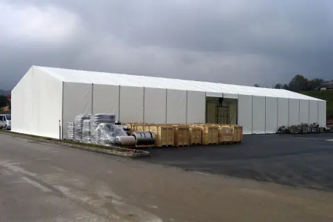 Ampia tensostruttura bianca, con merci stoccate all'esterno. Ottenere i permessi per queste strutture è fondamentale per la logistica.