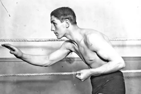 Georges Carpentier, a legendary boxer, poses in the ring, his muscular physique ready for action.