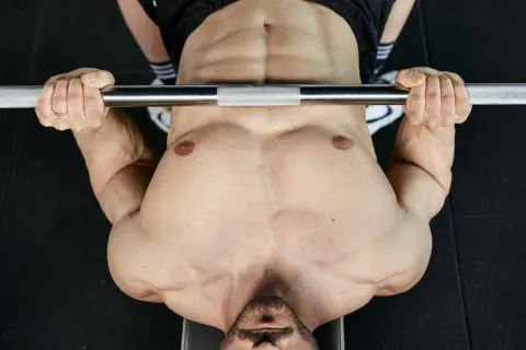 Uomo con pettorali definiti e addominali scolpiti solleva un bilanciere durante un allenamento in palestra.
