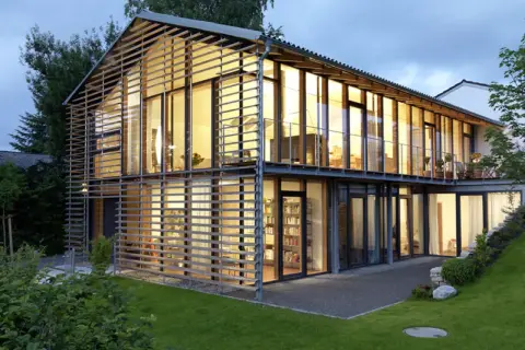Modernes Haus mit Satteldach, das durch eine Glasfassade und horizontale Lamellen eine neue Interpretation erfährt.