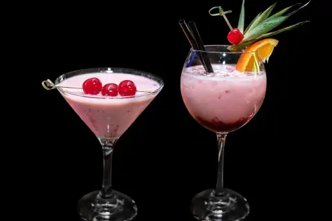 Dwa różowe drinki, jeden w kieliszku martini z wiśniami, drugi w kieliszku typu goblet z owocami. Zastanawiasz się, ile kalorii ma wódka smakowa?