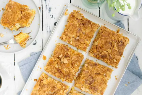 Saftiger butterkuchen ohne hefe, bestreut mit knusprigen Mandelblättchen. Ein Stück auf einem Teller mit einer Gabel.