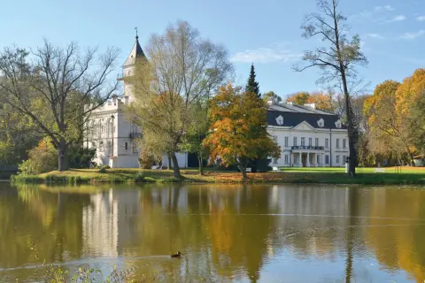 Pałac w jesiennej scenerii nad jeziorem, część Bolimowskiego Parku Krajobrazowego. Kaczka pływa po wodzie.