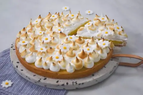 Une délicieuse tarte citron meringuée, ornée de petites fleurs en sucre, prête à être dégustée.