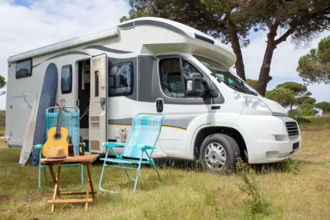 En vit husbil, en personbil klass 2, står parkerad i gräset. Surfbrädor, en gitarr och campingstolar antyder en avkopplande semester.