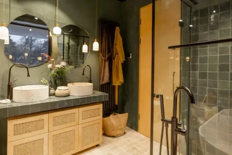 Bagno stile boho chic con doppio lavabo in pietra, mobili in legno e vimini, specchi irregolari e doccia con piastrelle verdi.