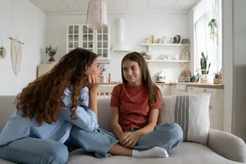 Mama rozmawia z nastolatką o zasadach w domu. Dziewczyna siedzi na kanapie, słuchając uważnie.
