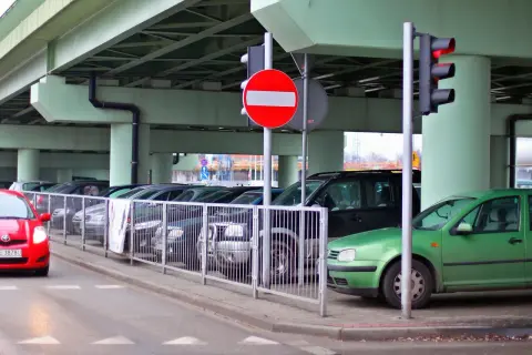 Czerwony samochód zbliża się do parkingu, gdzie stoi znak b2. Zielony samochód zaparkowany jest pod wiaduktem.