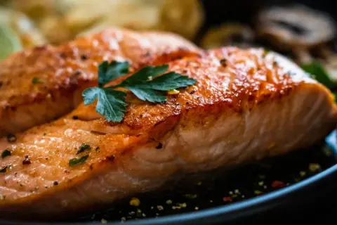 Zwei saftige Filets von gekochtem Lachs, garniert mit Petersilie und Gewürzen, liegen auf einem Teller neben Pilzen und Zitronenscheiben.