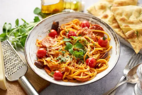 Pyszny makaron z chorizo, pomidorkami koktajlowymi i świeżą bazylią, posypany parmezanem. Idealny na szybki obiad.