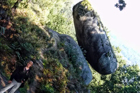 Hombre sonriente junto a una roca suspendida, un ejemplo de la pena do equilibrio en la naturaleza.