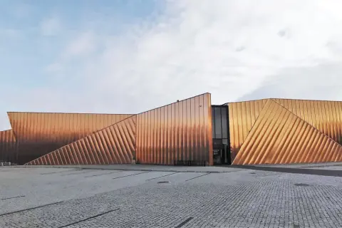 Nowoczesny budynek muzeum ognia z miedzianą elewacją, przypominającą płomienie.