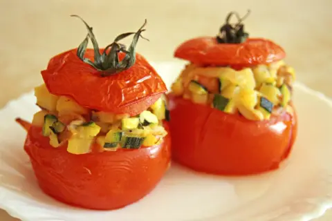 Deux tomates farcies, garnies d'un mélange de légumes et de fromage, sont présentées sur une assiette blanche.