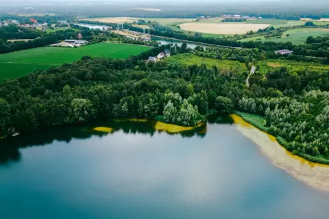Widok z lotu ptaka na spokojne, turkusowe wody, otoczone bujną zielenią lasów i pól. To miejsce, gdzie można poczuć spokój i podziwiać najczystsze jezioro w Polsce.