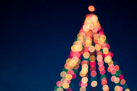 Luci natalizie sfocate creano la forma di un albero su sfondo blu scuro.