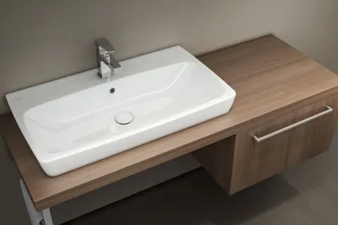 Elegancka, prostokątna misa umywalka nablatowa z chromowaną baterią, umieszczona na drewnianym blacie.