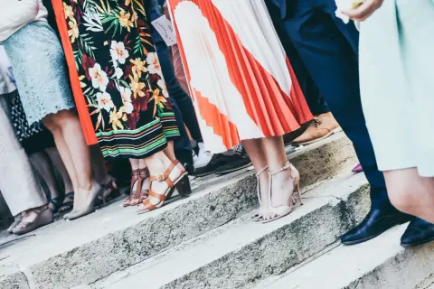 Gäste in festlicher Kleidung, die den **Dresscode Hochzeit** erfüllen, stehen auf einer Steintreppe. Bunte Kleider und elegante Schuhe.