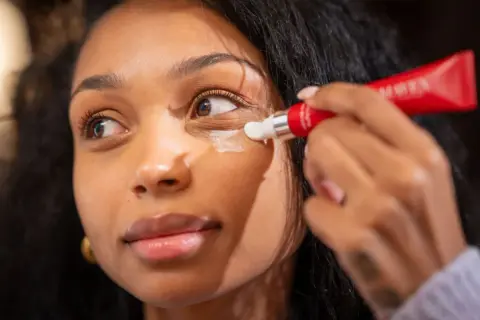 Donna applica crema contorno occhi per contrastare i segni sotto gli occhi, con un tubetto rosso.