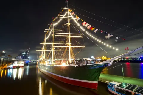 Großes Segelschiff mit Lichterketten und Flaggen im Hamburger Hafen bei Nacht, ein Highlight der museumsnacht hamburg.