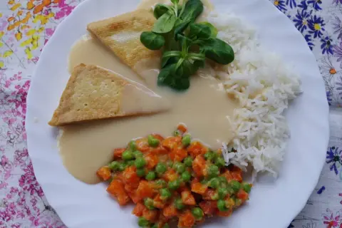 Talerz z ryżem, warzywami i dwoma trójkątnymi kawałkami czegoś w kremowym sosie. Idealny sos do ryżu!