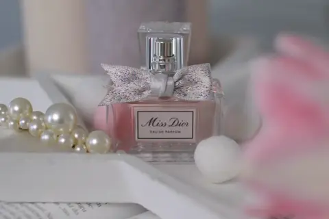 Elegancka butelka Miss Dior 100ml z kokardką, otoczona perłami i delikatnymi, białymi kulkami.