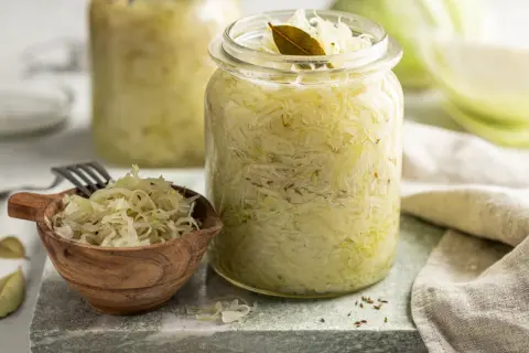 Frisches Sauerkraut im Glas, bereit für ein leckeres Sauerkraut Rezept. Ein kleiner Holzlöffel mit Sauerkraut und Lorbeerblätter liegen daneben.