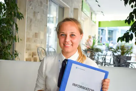 Uśmiechnięta rezydentka z niebieskimi oczami trzyma segregator z napisem "Informator".