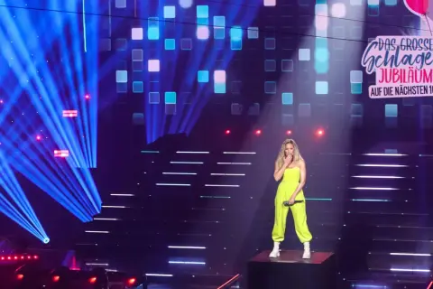 Eine Sängerin steht auf einer Bühne, umgeben von blauen Lichtstrahlen und einem LED-Bildschirm, der "Das große Schlager-Jubiläum" zeigt. Sie ist eine der vielen Schlagerstars Deutschlands.