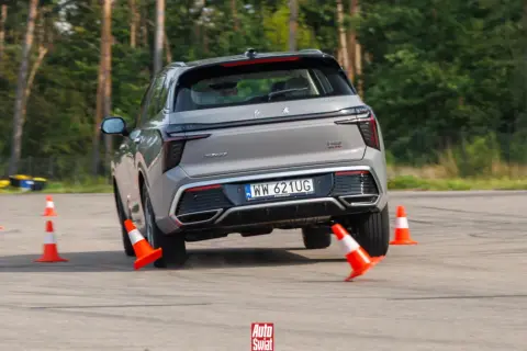 Szary SUV wykonuje test łosia, gwałtownie skręcając między pomarańczowymi pachołkami na torze.