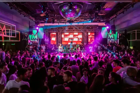 En stor publik njuter av 30 års fest aktiviteter med DJ och discokula. Ljusshow i lila och rosa skapar en festlig stämning.