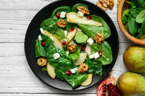 Sałatka z granatem, gruszką, orzechami i serem feta na talerzu. Pyszne połączenie smaków i kolorów.