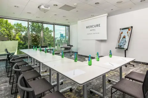 Sala konferencyjna w hotelu Mercure Poznań Centrum gotowa na spotkanie. Stoły ustawione, woda czeka, a za oknem zieleń.