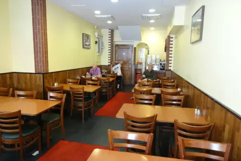 Interiör av en turkisk restaurang i Stockholm. Flera bord med trästolar och röda mattor. Tre gäster sitter vid borden.