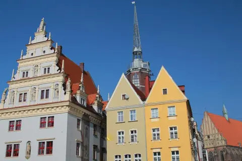 Kolorowe kamienice i wieża kościelna na rynku w Nysie pod błękitnym niebem.