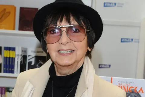 Halina Kunicka, w okularach i kapeluszu, prezentuje swoje piosenki alfabetycznie.