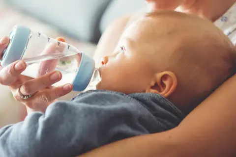 Mama próbuje nakarmić butelką dziecko, które nie chce pić wody.