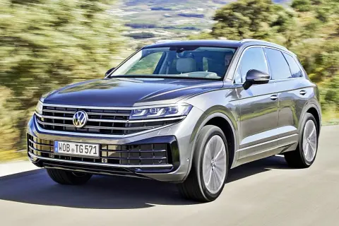 Szary Volkswagen Touareg pędzi po drodze, otoczony zielenią.