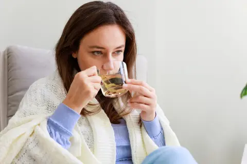 Kobieta pije napar z ziół, który może pomóc na biegunkę. Otulona kocem, szuka ulgi w domowym zaciszu.