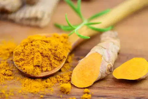 Kurkuma-Pulver auf einem Holzlöffel und frische Wurzeln. Kurkuma kann bei Durchfall helfen.