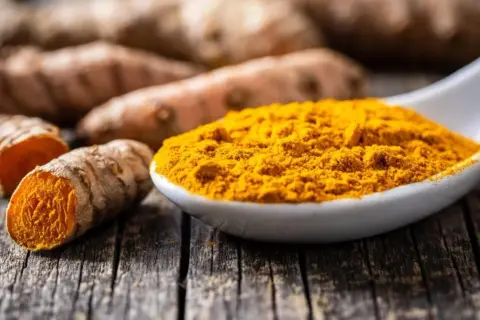 Frisch geschnittene Kurkumawurzeln und leuchtend gelbes Kurkumapulver auf einem Löffel. Die Kurkuma-Eigenschaften sind bekannt für ihre Farbe und ihren würzigen Duft.