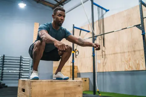 Man in squat position on a wooden box, preparing for explosive workouts.