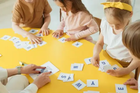 Dzieci ćwiczą pamięć fonologiczną, dopasowując litery na żółtym stole.