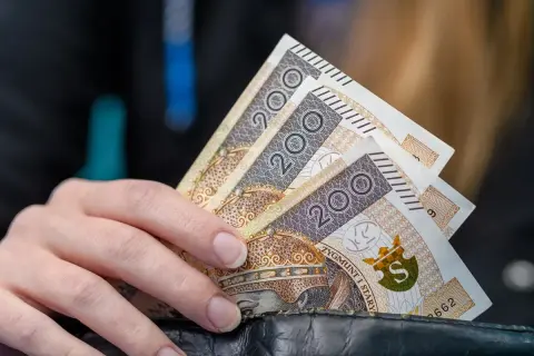 Dłoń trzyma banknoty 200 zł. Kto nie ma prawa do zasiłku dla bezrobotnych, musi radzić sobie sam.