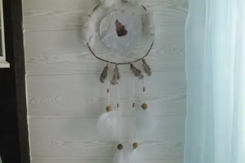 Un attrape rêve, ornement traditionnel, orné d'un loup hurlant, de plumes et de perles, suspendu devant un mur en bois clair.