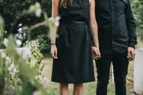 Ein Paar in schwarzer Kleidung, die Frau in einem schlichten Kleid, hält Händchen. Passende **Beerdigung Kleidung Frau Sommer** für einen traurigen Anlass.