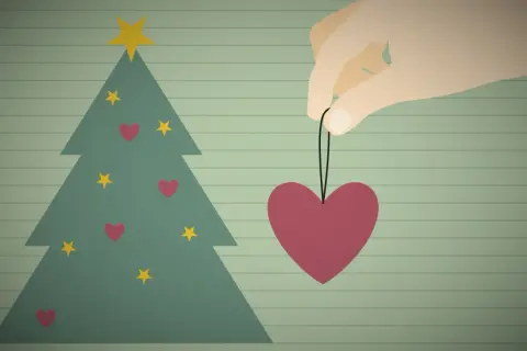 Ein Herz als Weihnachtsbaumschmuck, gehalten von einer Hand, symbolisiert eine besinnliche Weihnacht voller Liebe.